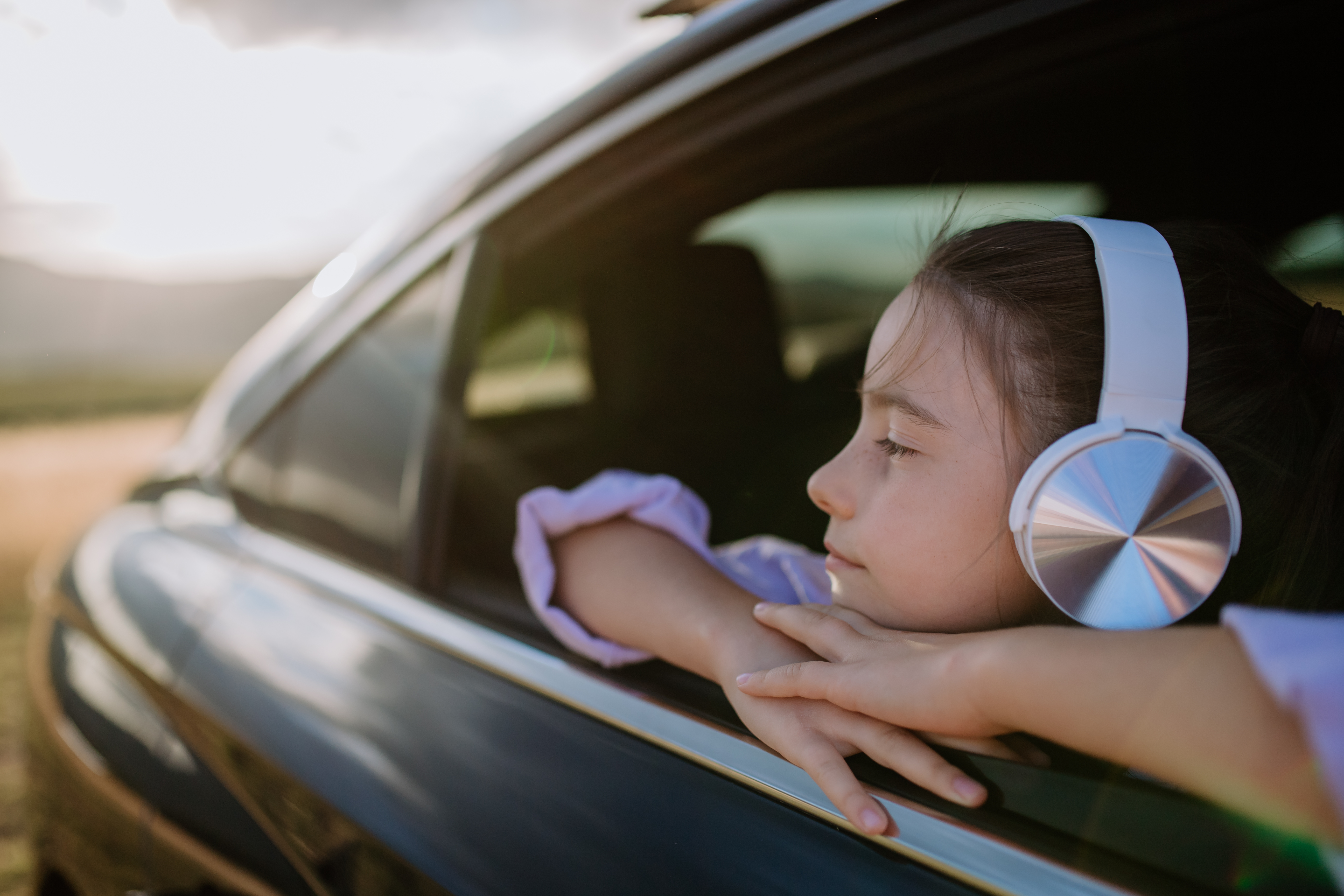 Young girl with headphones looking out car window during scenic drive
